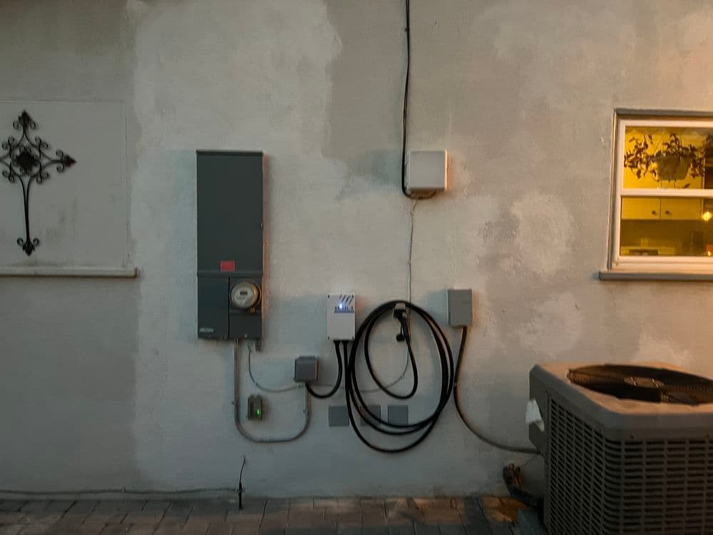 Electrical panel and outdoor AC unit mounted on a wall at twilight, highlighting key features.