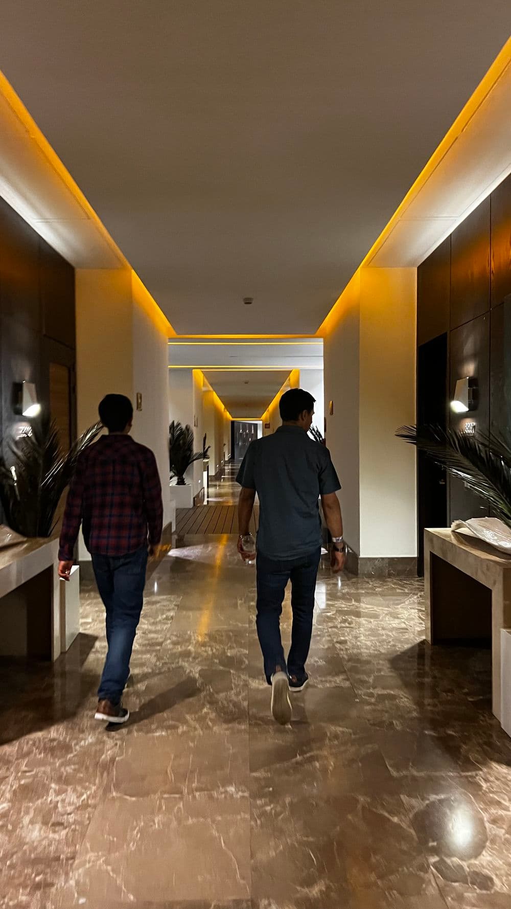Two men walking down a stylish hotel hallway with ambient lighting and modern decor.