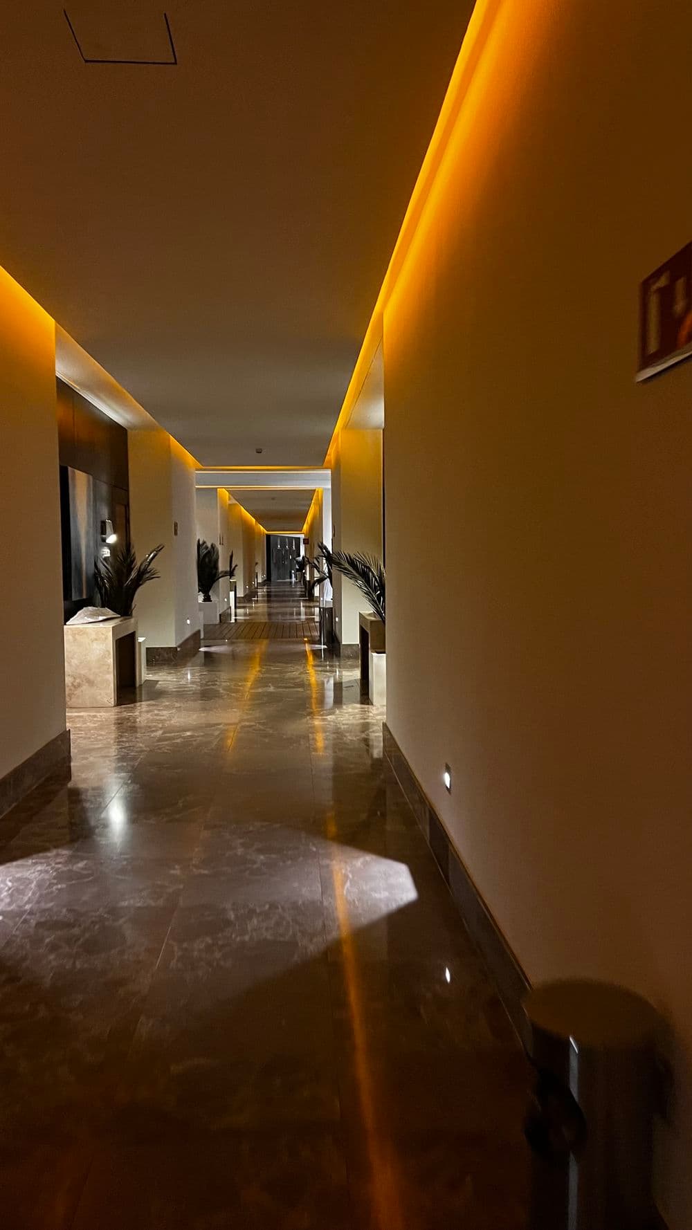 Illuminated hallway with warm lighting, marble floor, and modern decor in a luxury hotel.