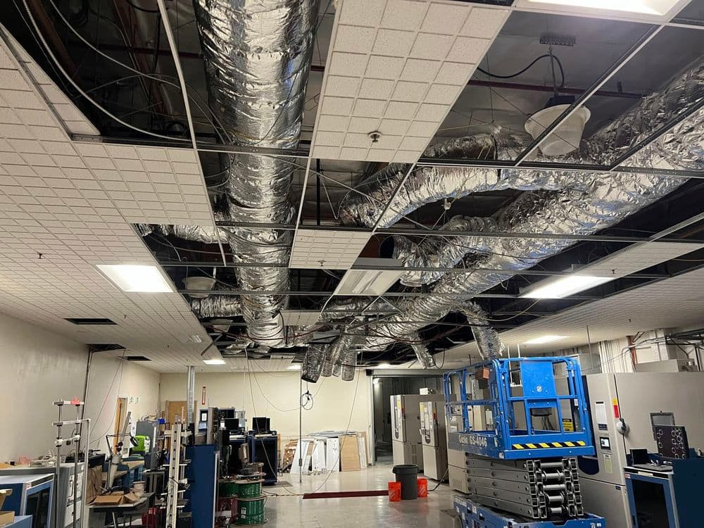 Exposed ductwork and ceiling tiles in a large industrial workspace.