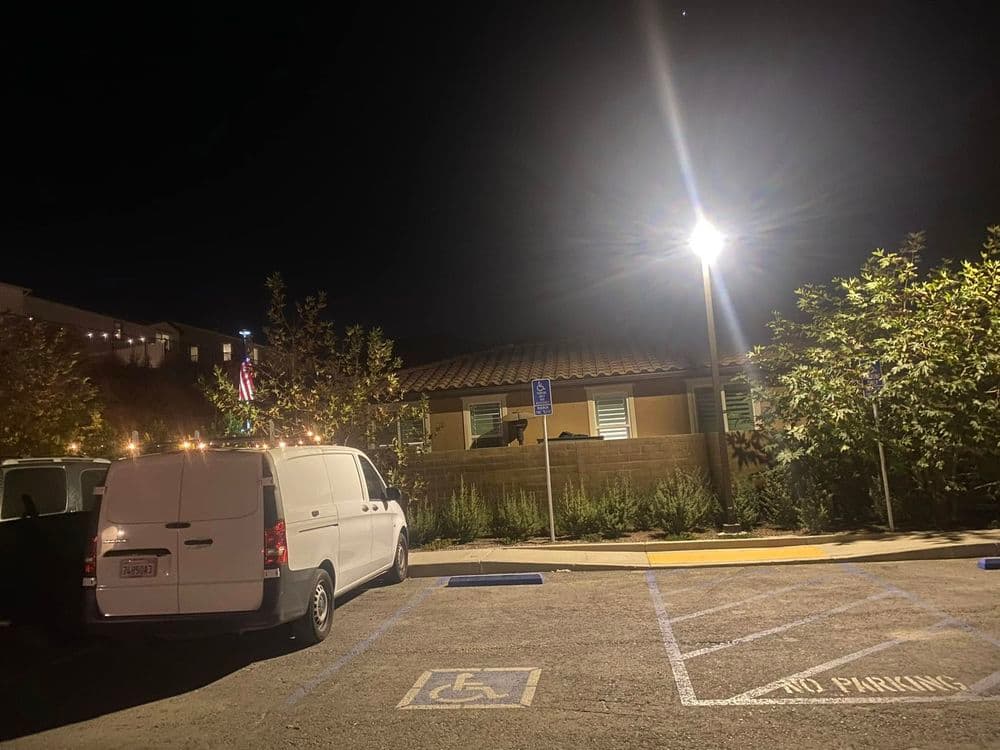 Van parked in well-lit lot at night, featuring accessible parking and greenery.