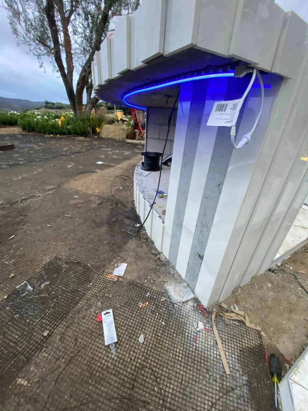 Modern kiosk with blue LED lighting, set in an outdoor area with scattered debris.